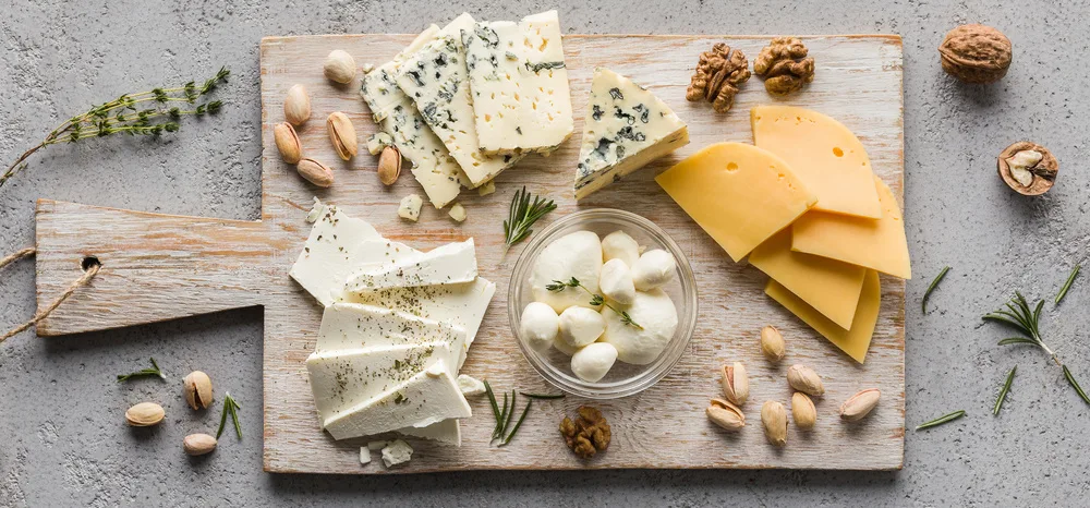 Assortment of cheese with nuts on wooden board over white concrete background, top view, panorama